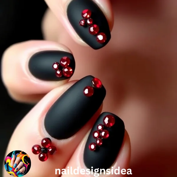 Matte black nails adorned with red rhinestones create a luxurious, festive look that suits any holiday occasion